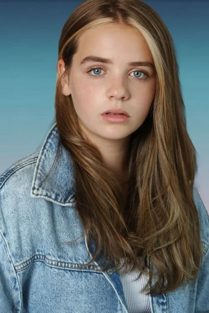 Head-and-shoulders portrait of a girl with long light-brown hair in a denim jacket against a blue background